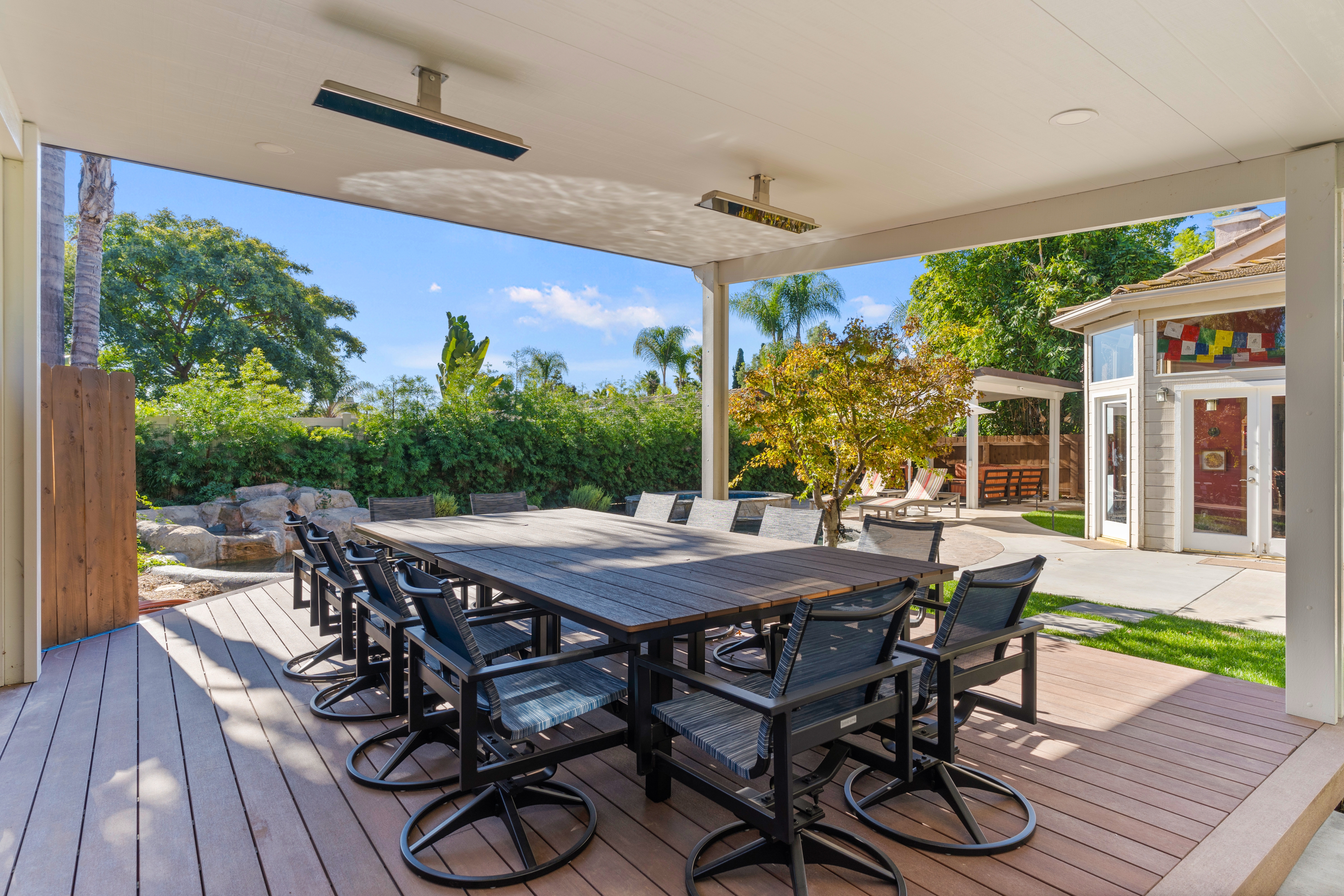 Covered composite deck with a large dining table, swivel chairs and ceiling-mounted heaters.