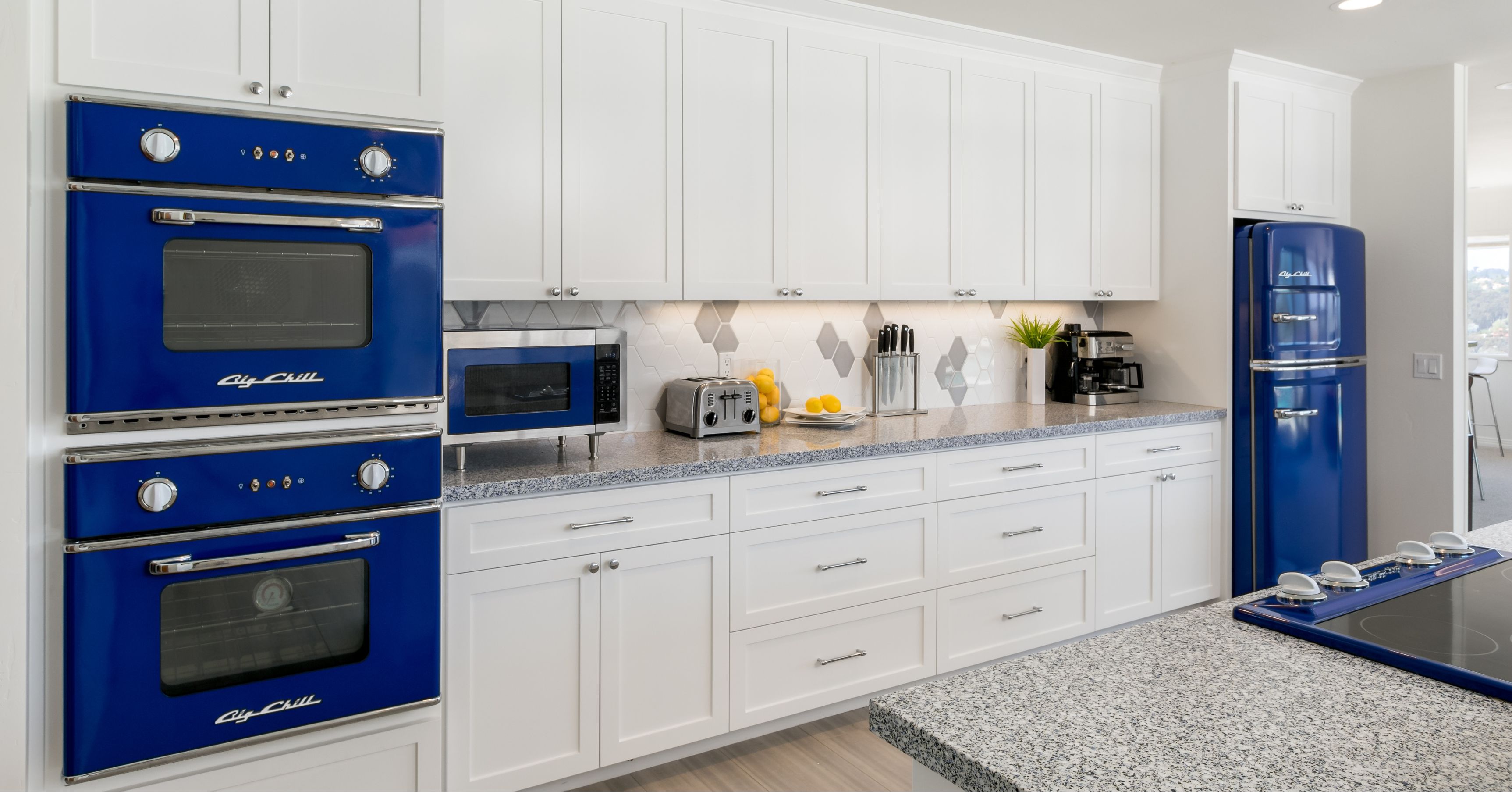 Custom white kitchen with blue retro appliances, shaker cabinets, quartz countertops, and geometric tile backsplash designed through a design-build process.
