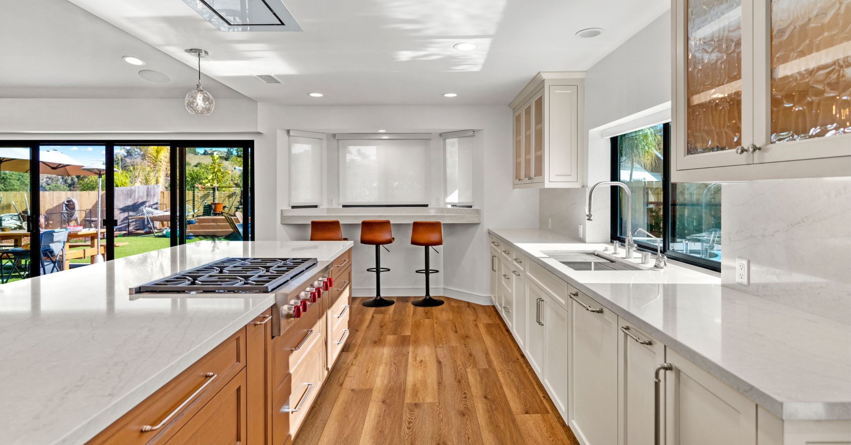 Spacious remodeled kitchen with a large wood island, gas cooktop, white countertops, and backyard-facing glass doors.