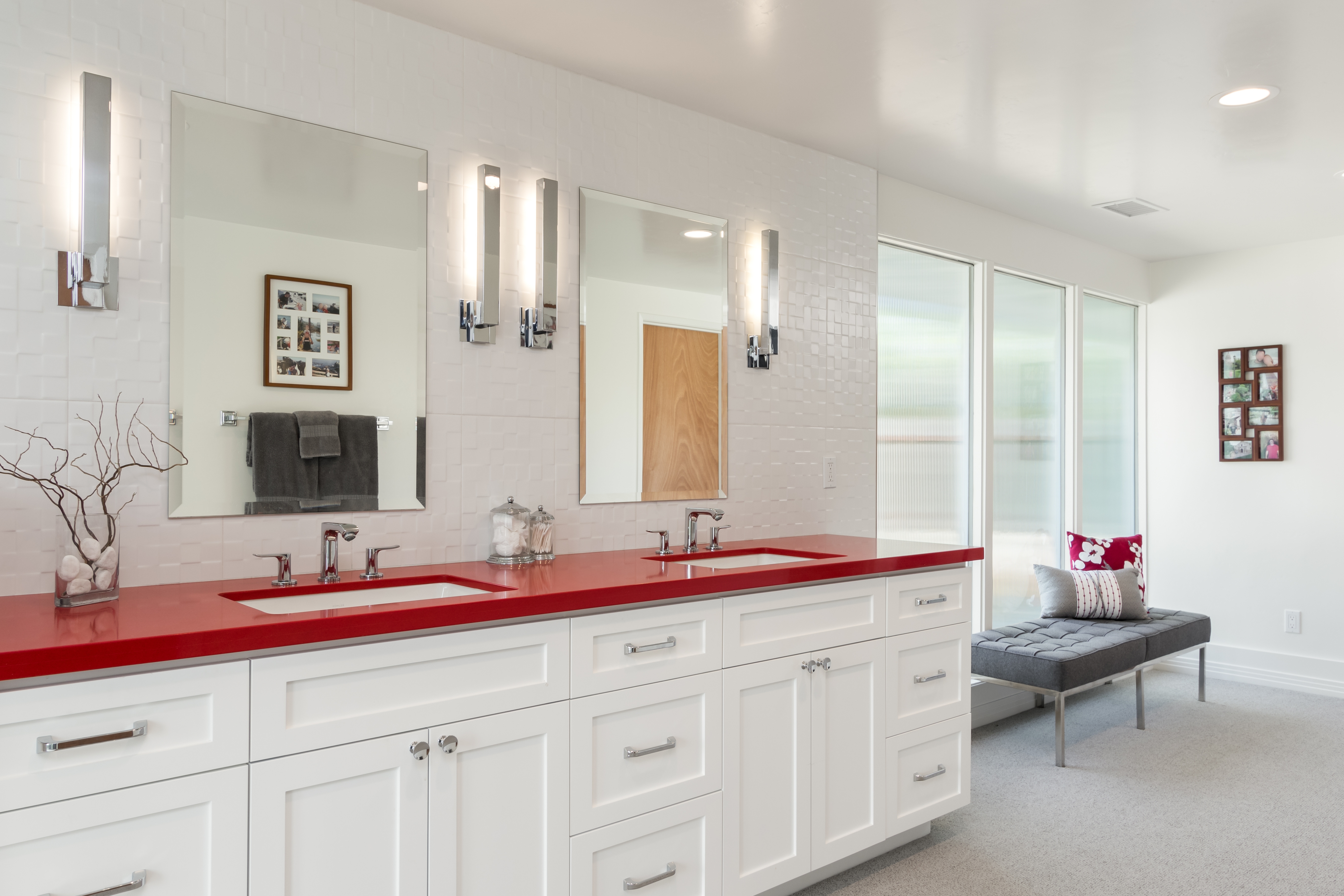 Double vanity with white cabinetry, red countertop, illuminated mirrors and textured tile.