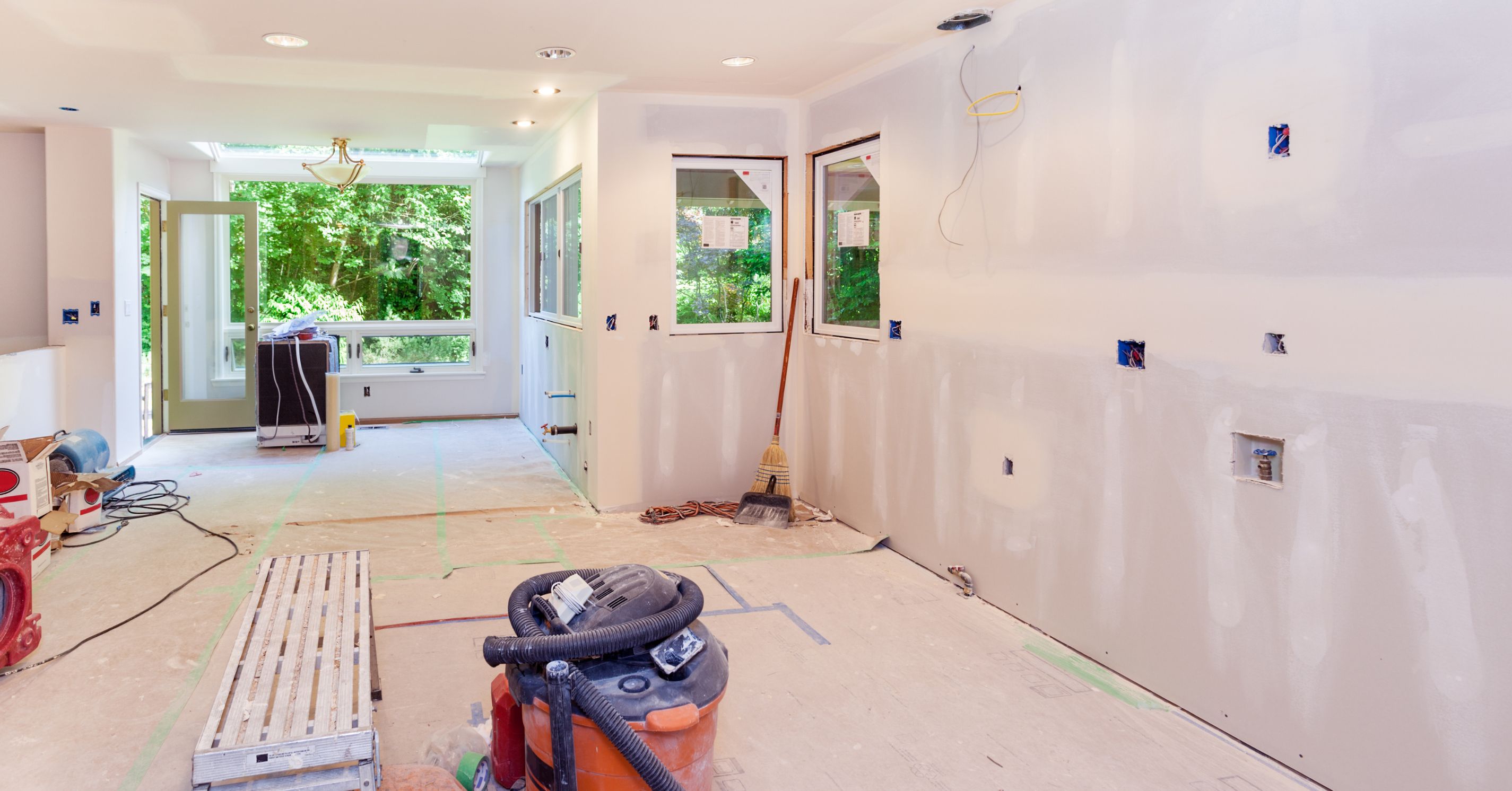 Interior home remodel during the drywall phase with newly finished walls, recessed lighting, electrical rough-ins, and construction equipment.