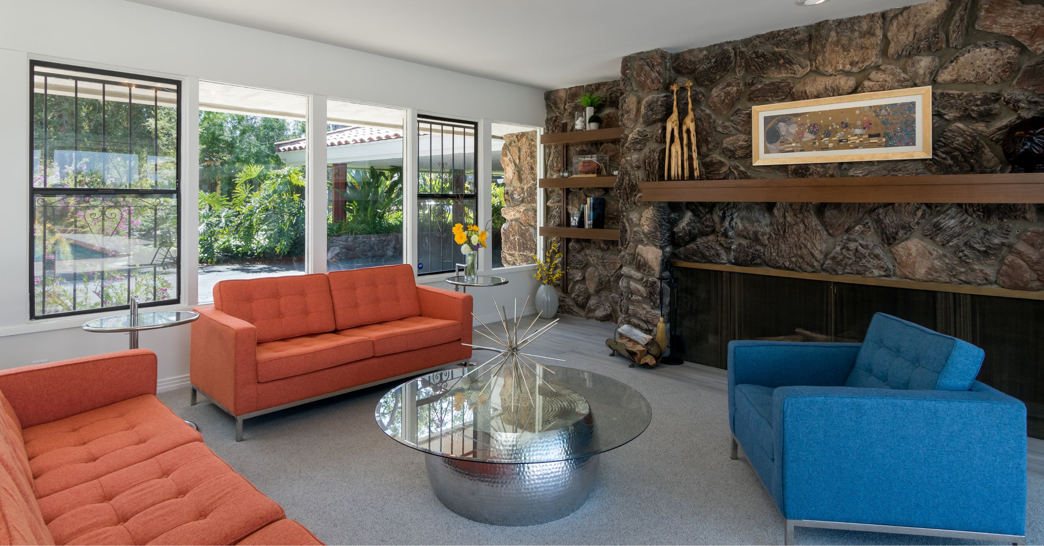 Contemporary living room remodel featuring a natural stone fireplace, large picture windows, modern furniture, and custom floating shelves.