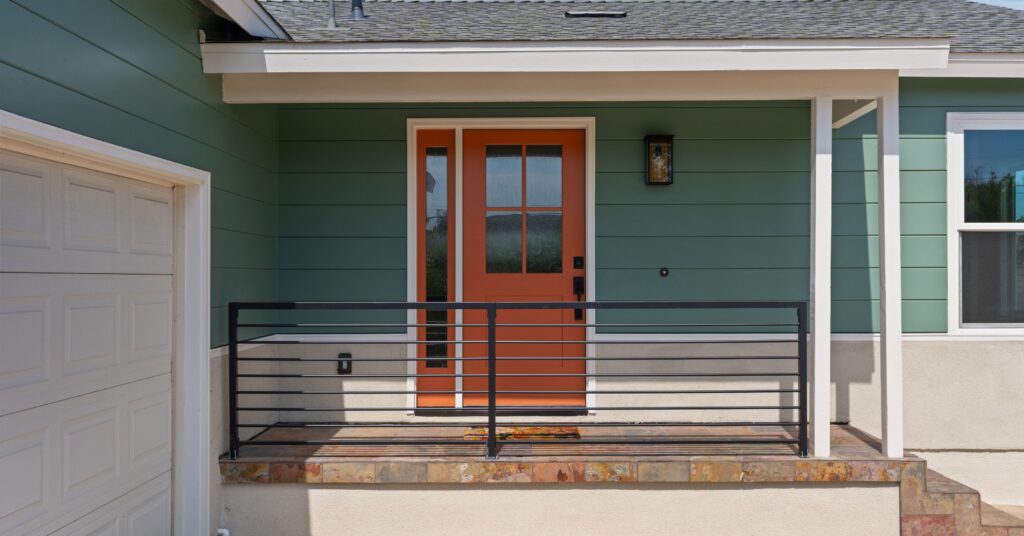 Front porch with modern orange entry door, covered porch, and accessible railing as part of a remodeled San Diego home addition.