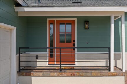 Front porch with modern orange entry door, covered porch, and accessible railing as part of a remodeled San Diego home addition.