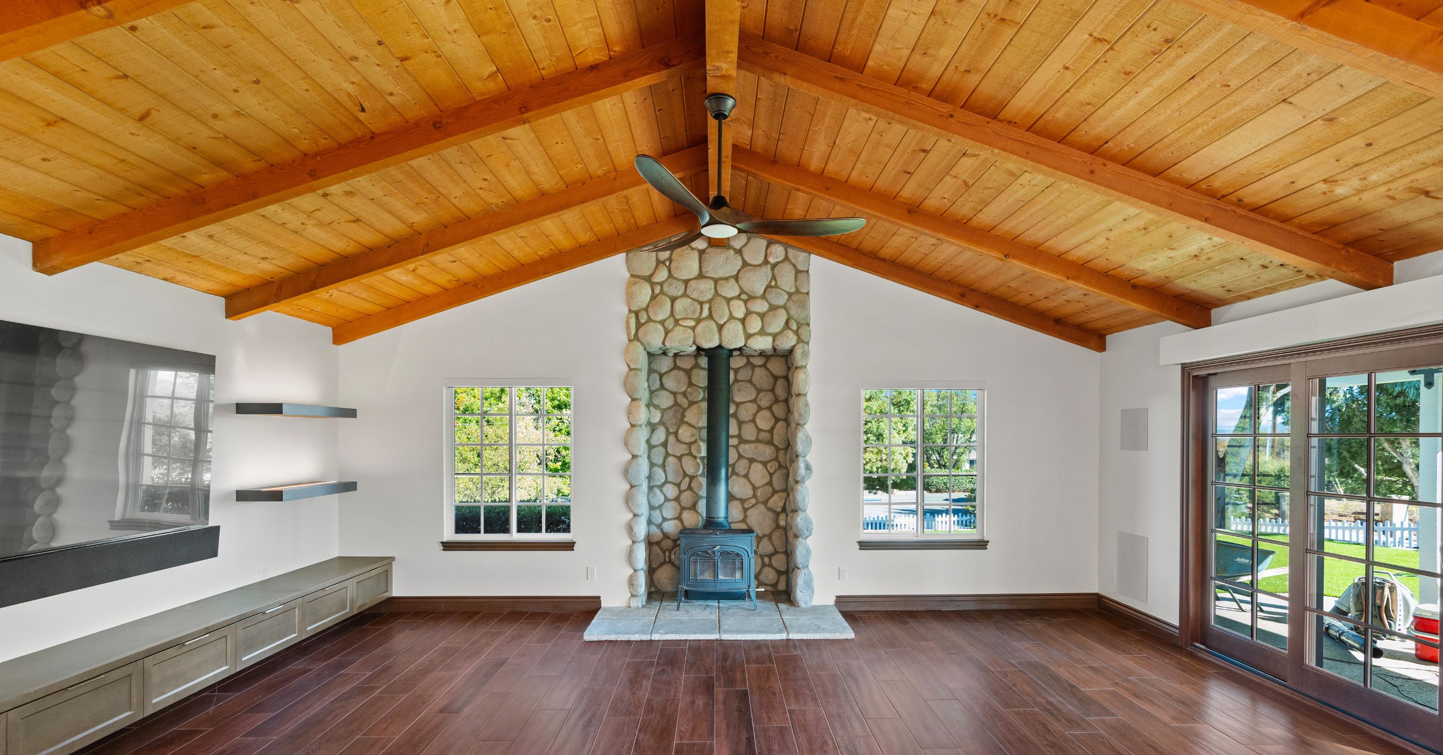 Finished living room remodel featuring vaulted wood ceilings, a stone fireplace, wood flooring, and built-in media cabinetry.