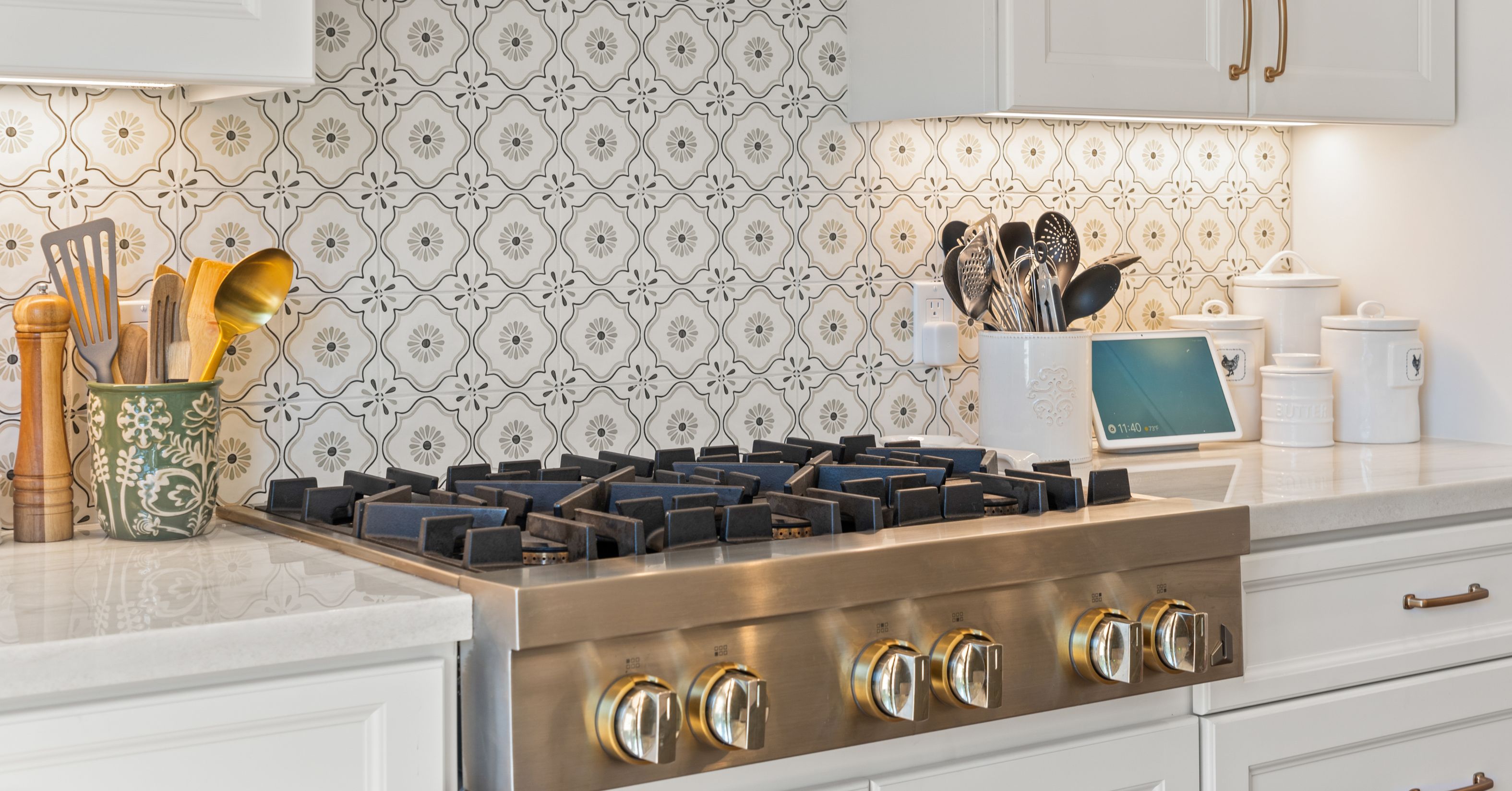 Modern gas range with large control knobs, white cabinetry, and decorative tile backsplash in an accessible kitchen designed for aging in place.
