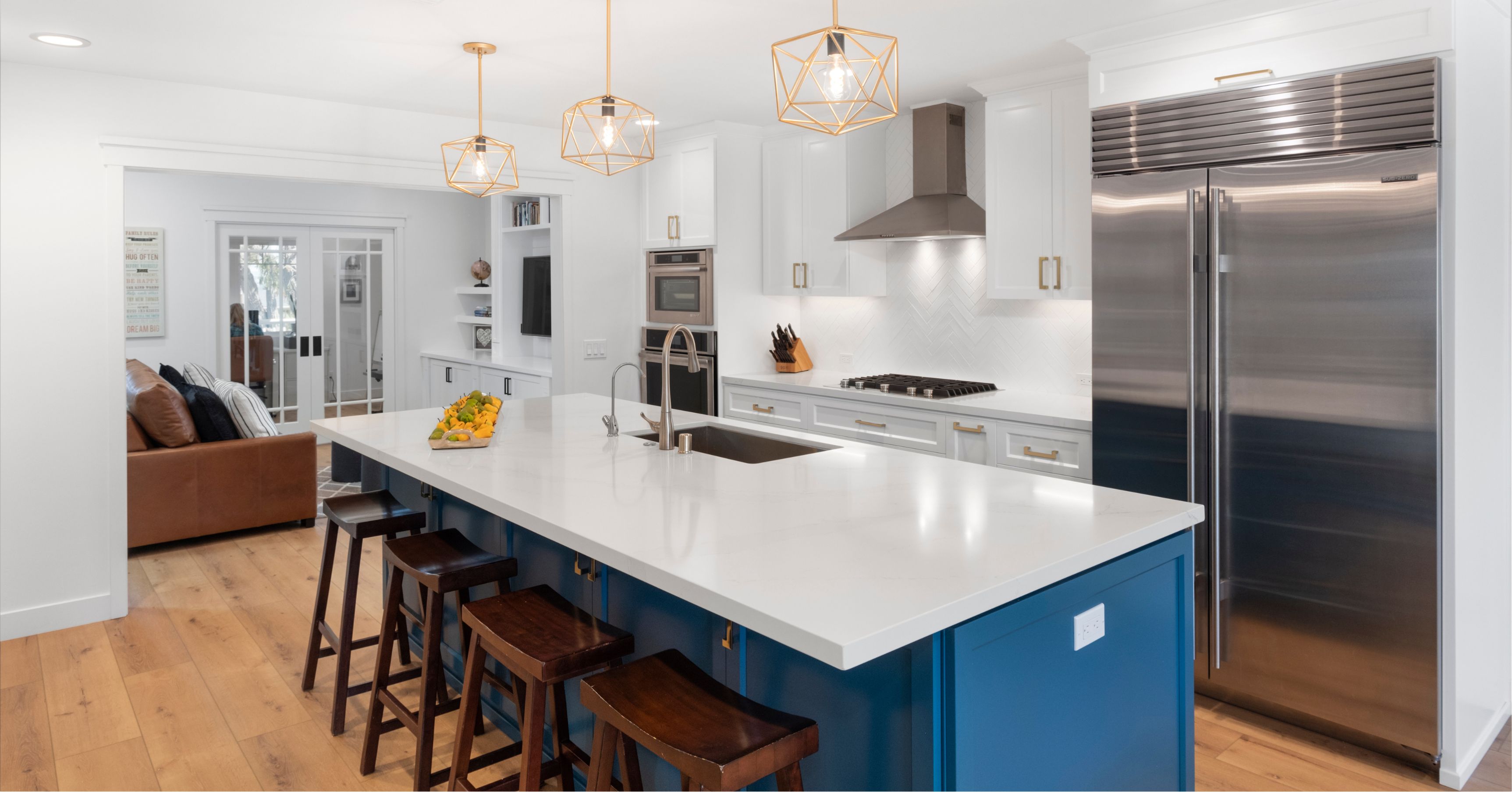 Modern white kitchen with blue island, quartz countertops, stainless steel appliances, custom cabinetry, and pendant lighting after a complete renovation.
