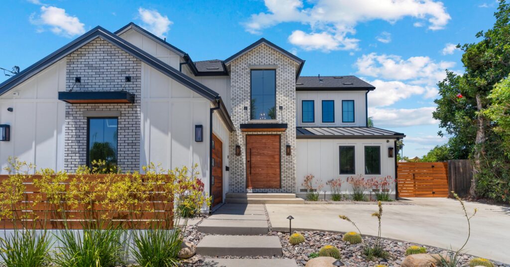 Front exterior of a contemporary two-story San Diego home remodeled with a primary suite addition, white brick façade, modern wood entry door, and updated landscaping.