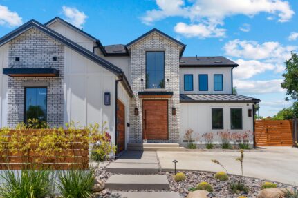 Front exterior of a contemporary two-story San Diego home remodeled with a primary suite addition, white brick façade, modern wood entry door, and updated landscaping.