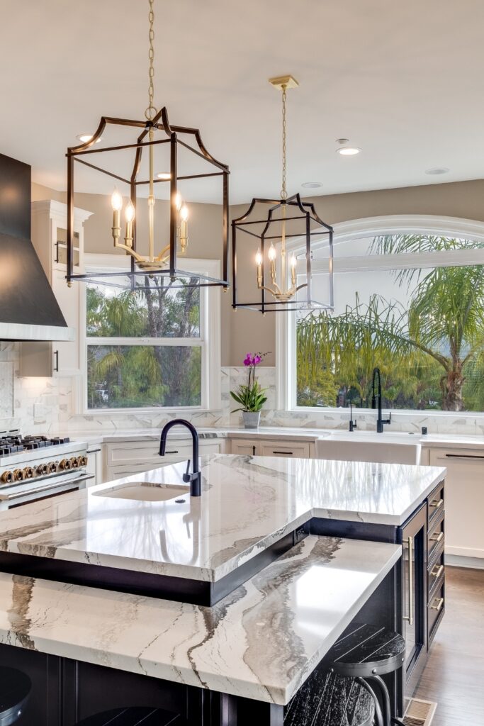 Alpine kitchen remodel with a tiered stone island, black cabinetry, white perimeter cabinets, farmhouse sink, and oversized lantern pendants.