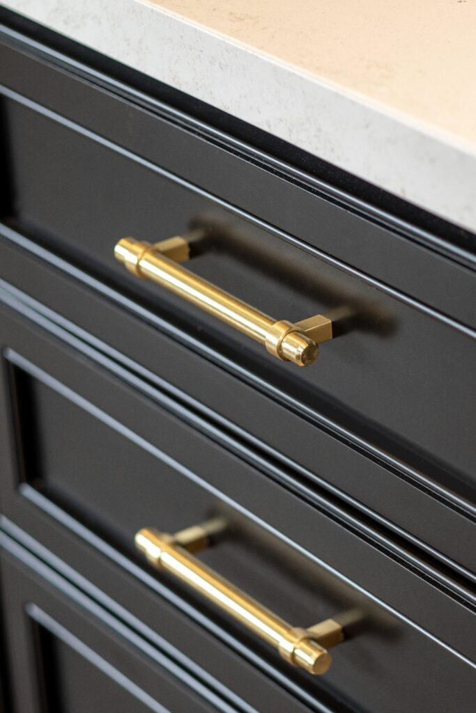 Close-up of brass cabinet pulls installed on black shaker-style kitchen drawers.