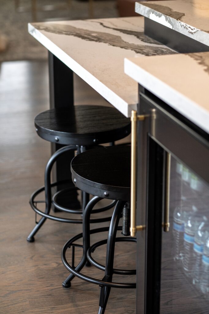 Tiered stone island seating area with black stools, brass hardware, and an integrated beverage refrigerator.