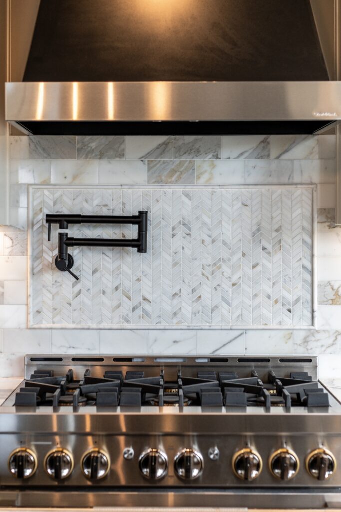 Professional gas range with a black vent hood, marble tile backsplash, and wall-mounted pot filler in the Carpenter kitchen.
