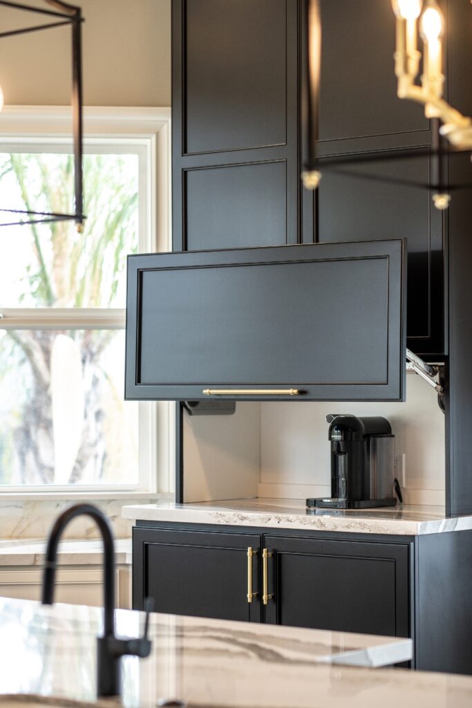 Built-in black coffee station with a lift-up cabinet door, brass hardware, and stone countertop.