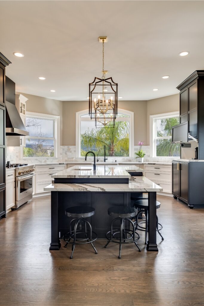 Front view of the Carpenter kitchen with a black island, layered stone countertops, lantern lighting, and white perimeter cabinetry.