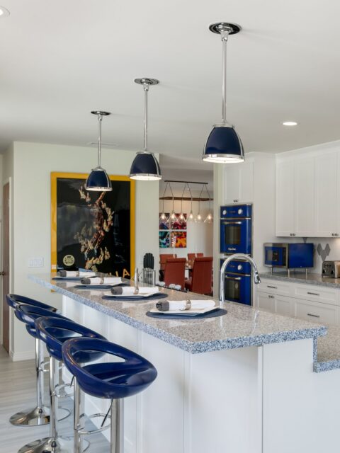 Bonita whole-home remodel kitchen with white shaker cabinets, granite island, blue seating, pendant lights and blue appliances.
