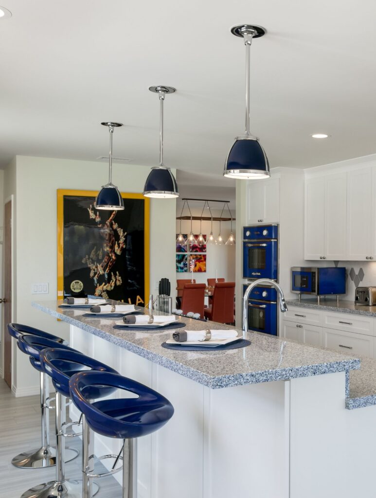 Bonita whole-home remodel kitchen with white shaker cabinets, granite island, blue seating, pendant lights and blue appliances.