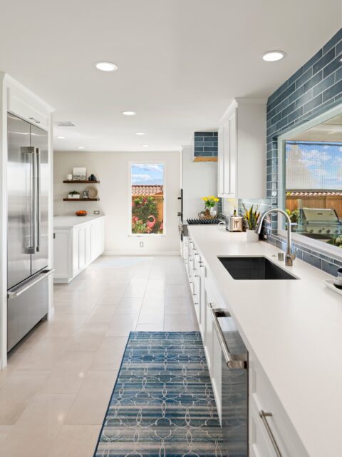 Bonita kitchen remodel with white Shaker cabinetry, long white counters, blue tile backsplash, stainless appliances and a windowed sink wall.