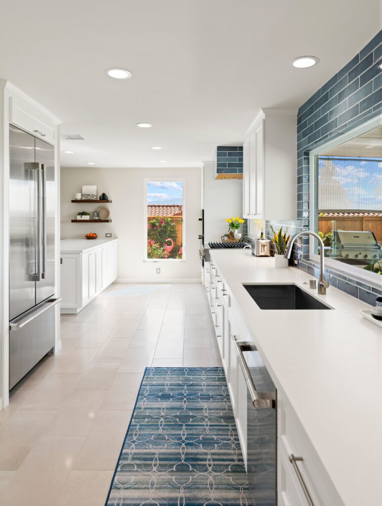 Bonita kitchen remodel with white Shaker cabinetry, long white counters, blue tile backsplash, stainless appliances and a windowed sink wall.