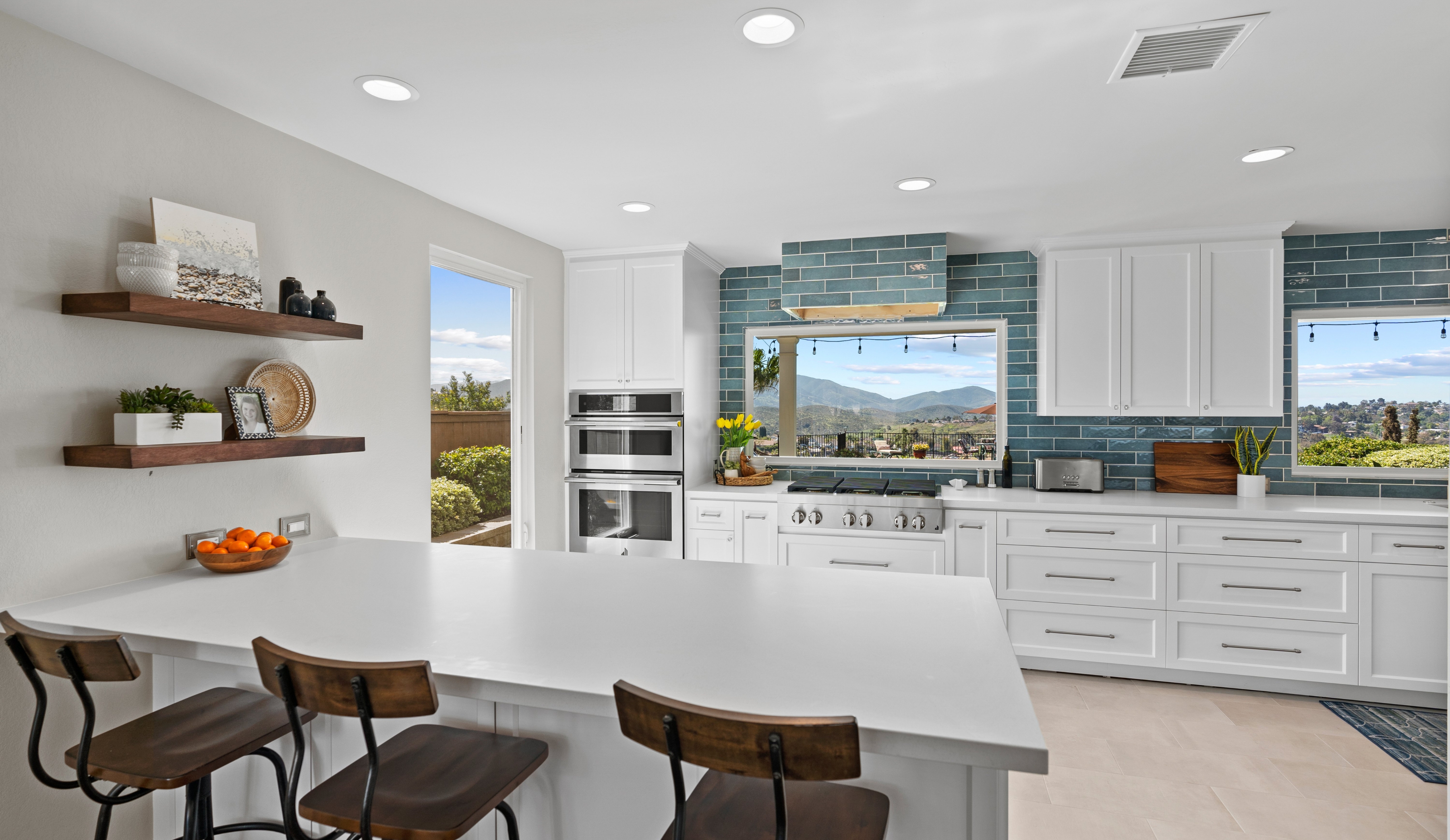 Open Bonita kitchen remodel with peninsula seating, white cabinetry, blue tile backsplash, double ovens and a range beneath view windows.
