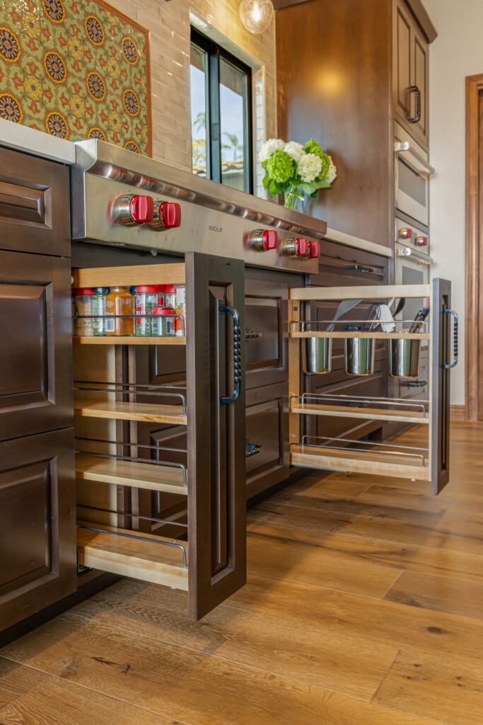 Pullout spice and utensil organizers beside a stainless range, set within dark wood kitchen cabinetry.