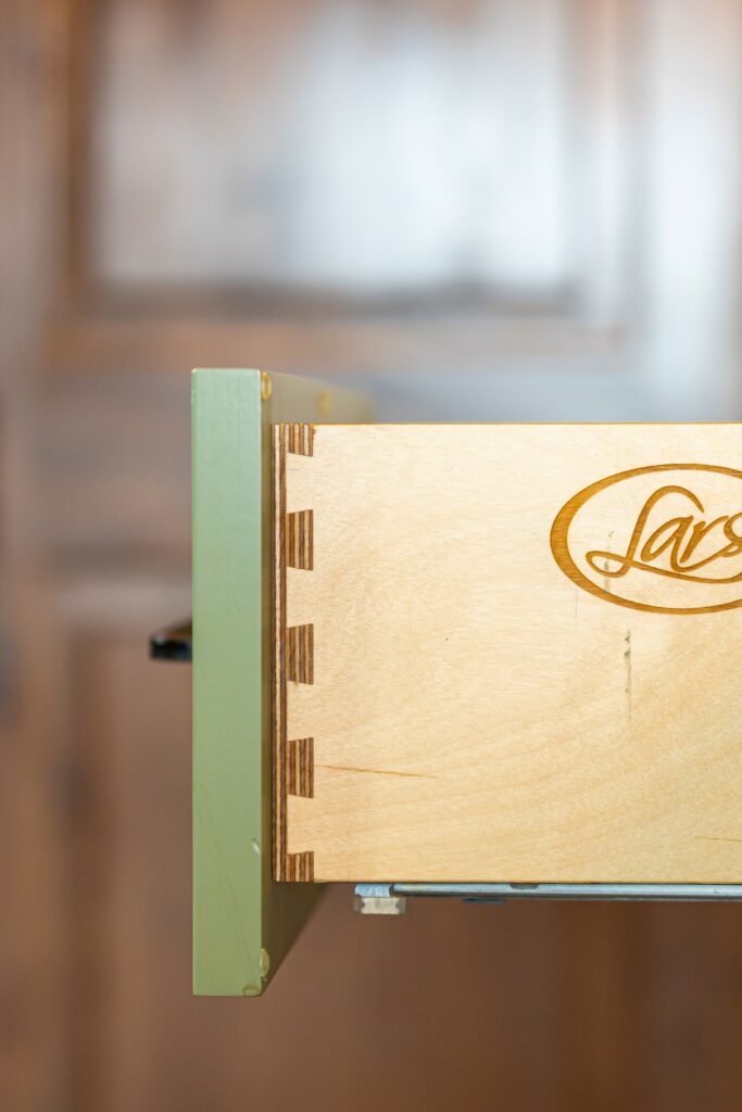 Custom dovetail drawer detail in green painted cabinetry with exposed layered wood construction.