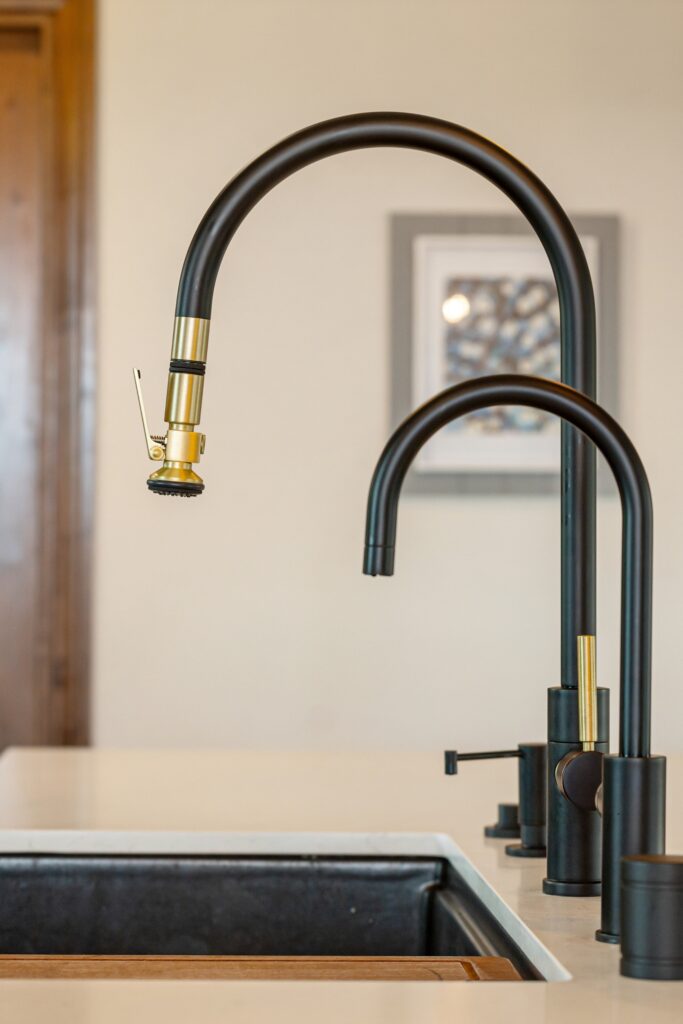 Black kitchen faucet with brass accents and a secondary faucet above a dark undermount sink.