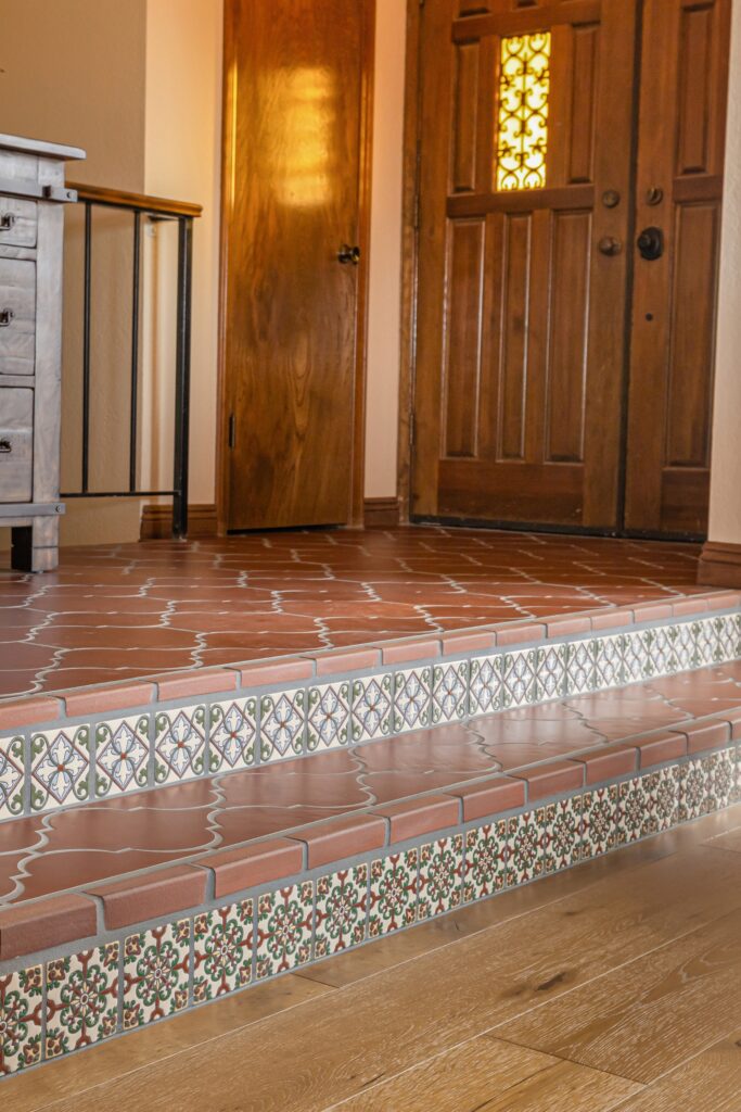 Terracotta entry steps with decorative Spanish tile risers, wood front door and black iron railing.