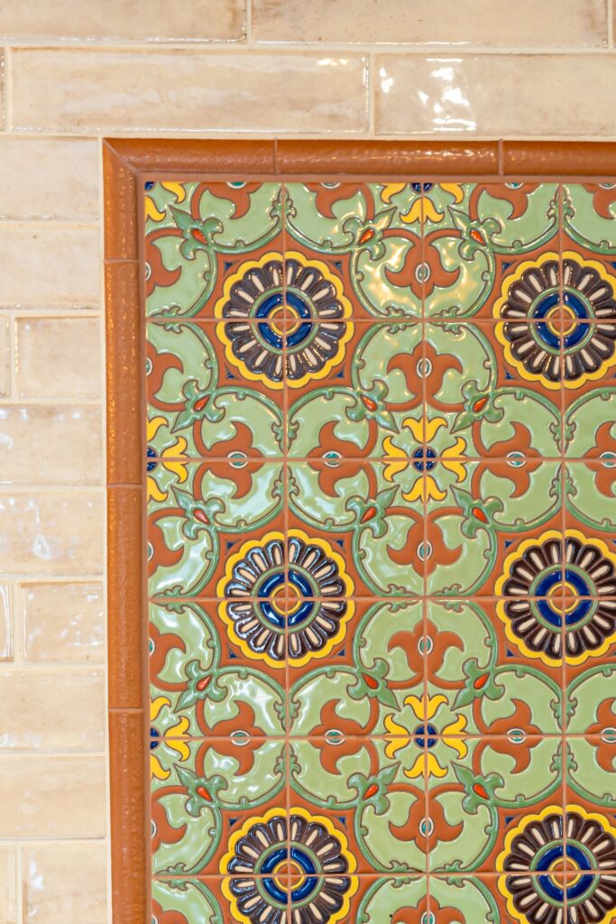 Colorful Spanish tile mural framed by terracotta trim within a glossy beige kitchen backsplash.