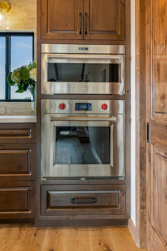 Stainless speed oven and wall oven built into dark wood cabinetry beside a wood pocket door.