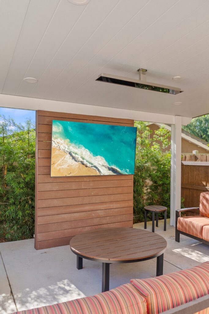 Poolside lounge with a wall-mounted TV, horizontal wood accent wall and ceiling-mounted heater.