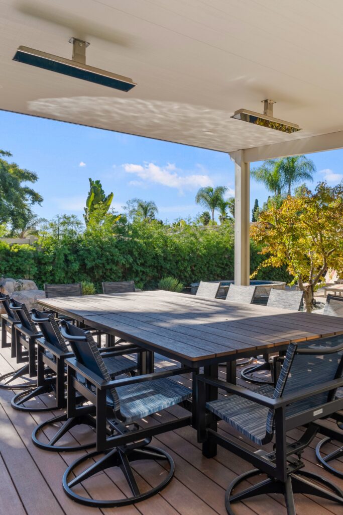 Composite deck dining area with a large table, swivel chairs, Alumawood cover and overhead heaters.