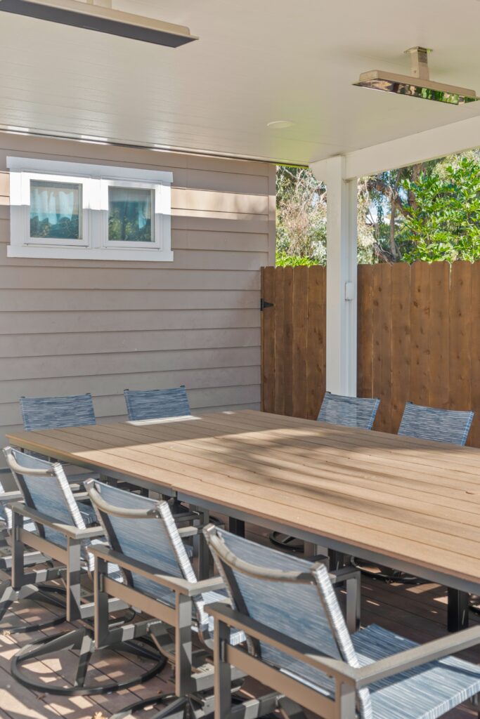Covered outdoor dining space with wood-look table, mesh chairs, composite decking and wood fencing.