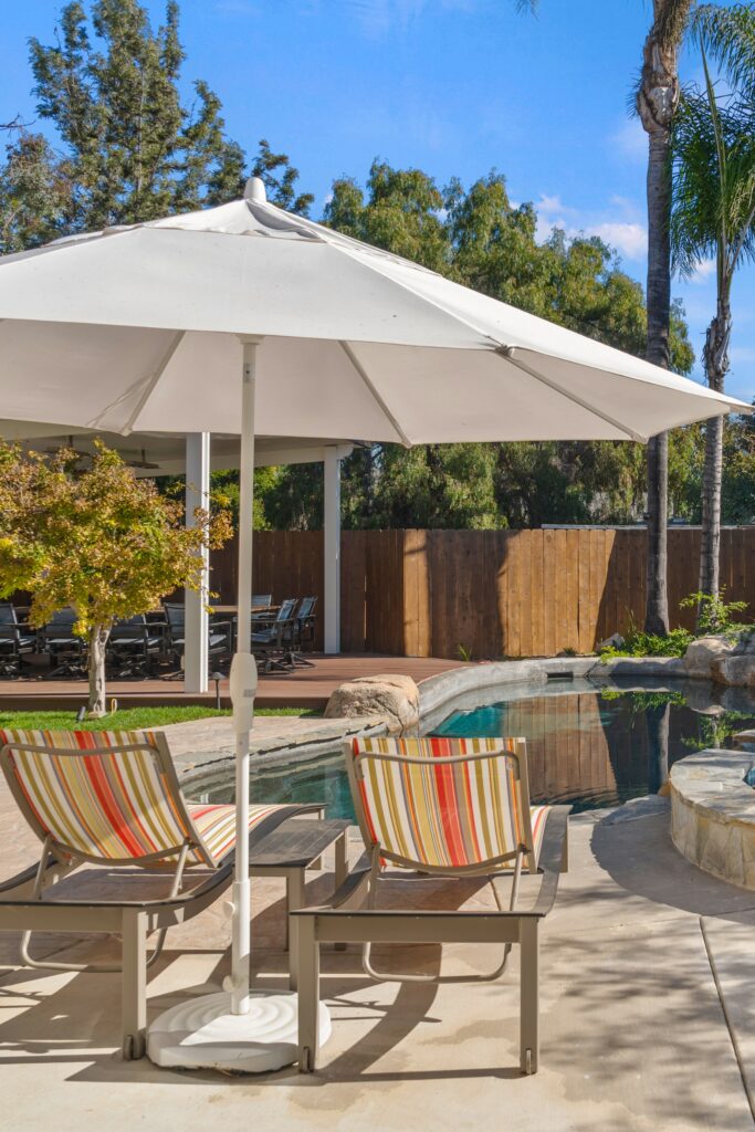 Poolside chaise lounges beneath a white umbrella with a covered composite deck dining area beyond.