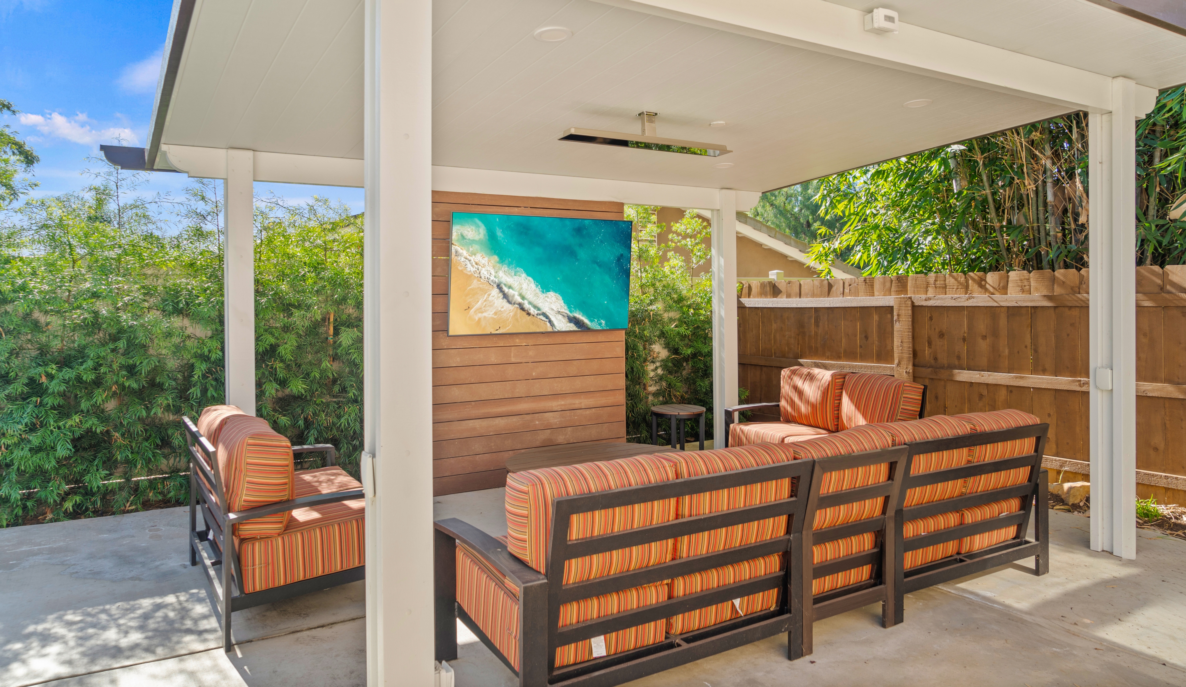 Covered Bonita poolside lounge with striped seating, concrete patio, ceiling-mounted heater and TV accent wall.