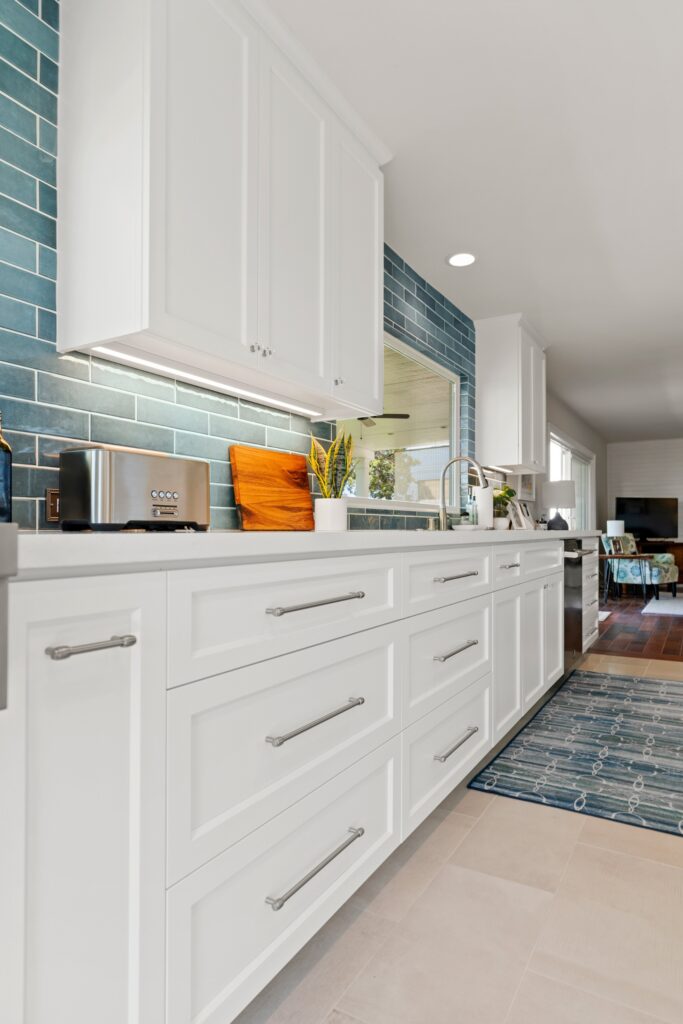 White Shaker drawers with brushed metal pulls, blue subway tile and undercabinet lighting.