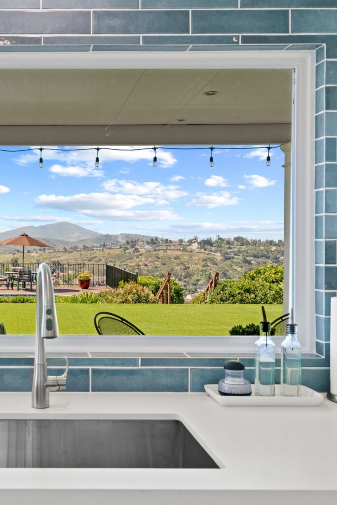 Stainless undermount sink below a picture window framed by blue tile with views of the hills in Bonita California.