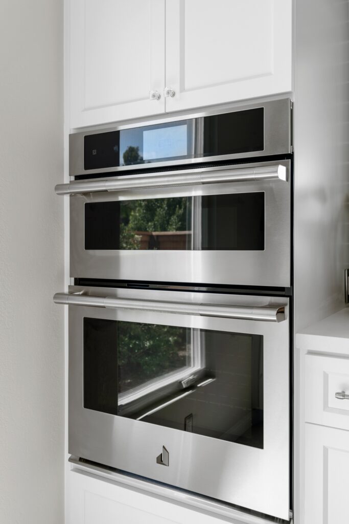 Stainless microwave and wall oven built into tall white Shaker cabinetry.