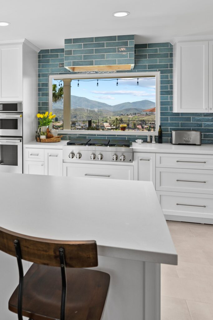 Kitchen peninsula with seating, white counters, six-burner range, blue tile and a large view window.