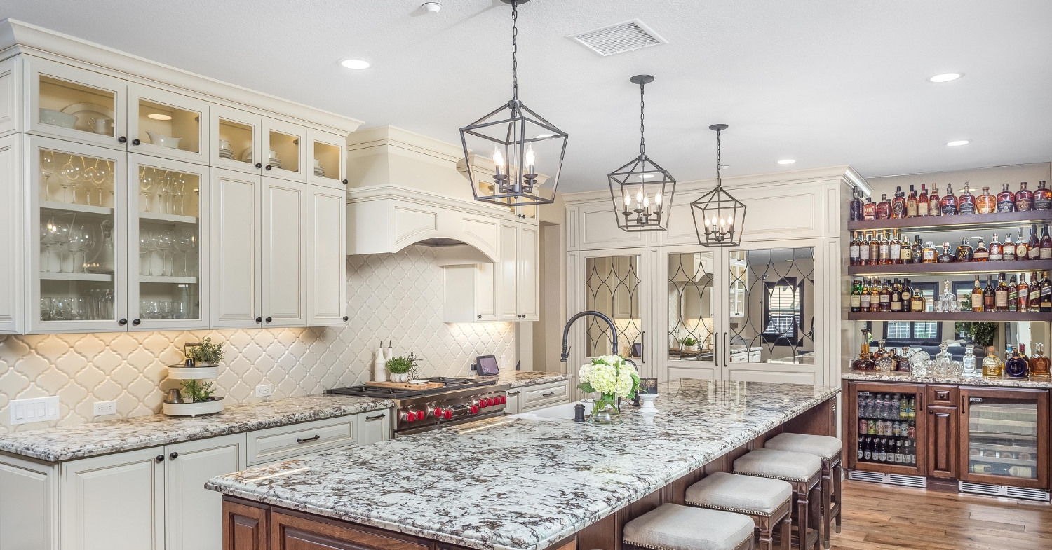 Custom kitchen with glass-front cabinets, a large granite island, professional range, built-in bar, and decorative lighting.