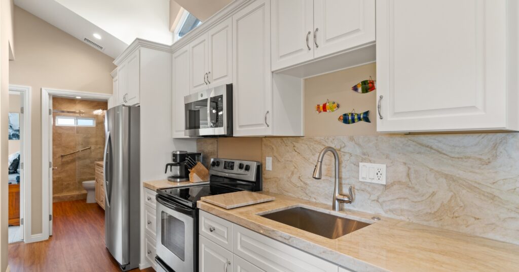 Remodeled galley kitchen with white cabinets, quartzite counters and full-height slab backsplash, with a tiled walk-in shower visible beyond.