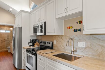 Remodeled galley kitchen with white cabinets, quartzite counters and full-height slab backsplash, with a tiled walk-in shower visible beyond.
