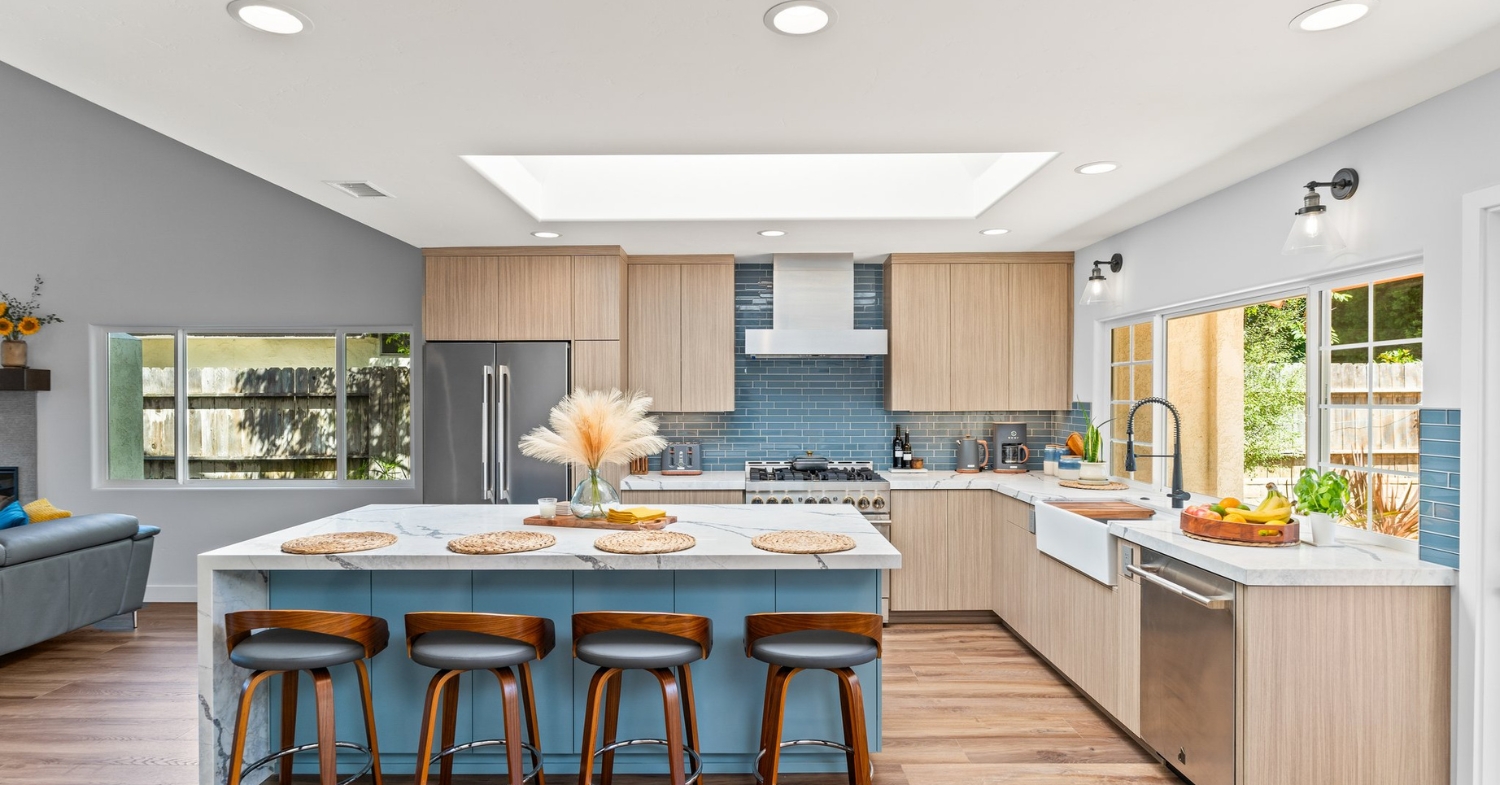 Bright remodeled kitchen with a blue island, white oak cabinets, quartz waterfall counters, blue glass tile backsplash and a new skylight.