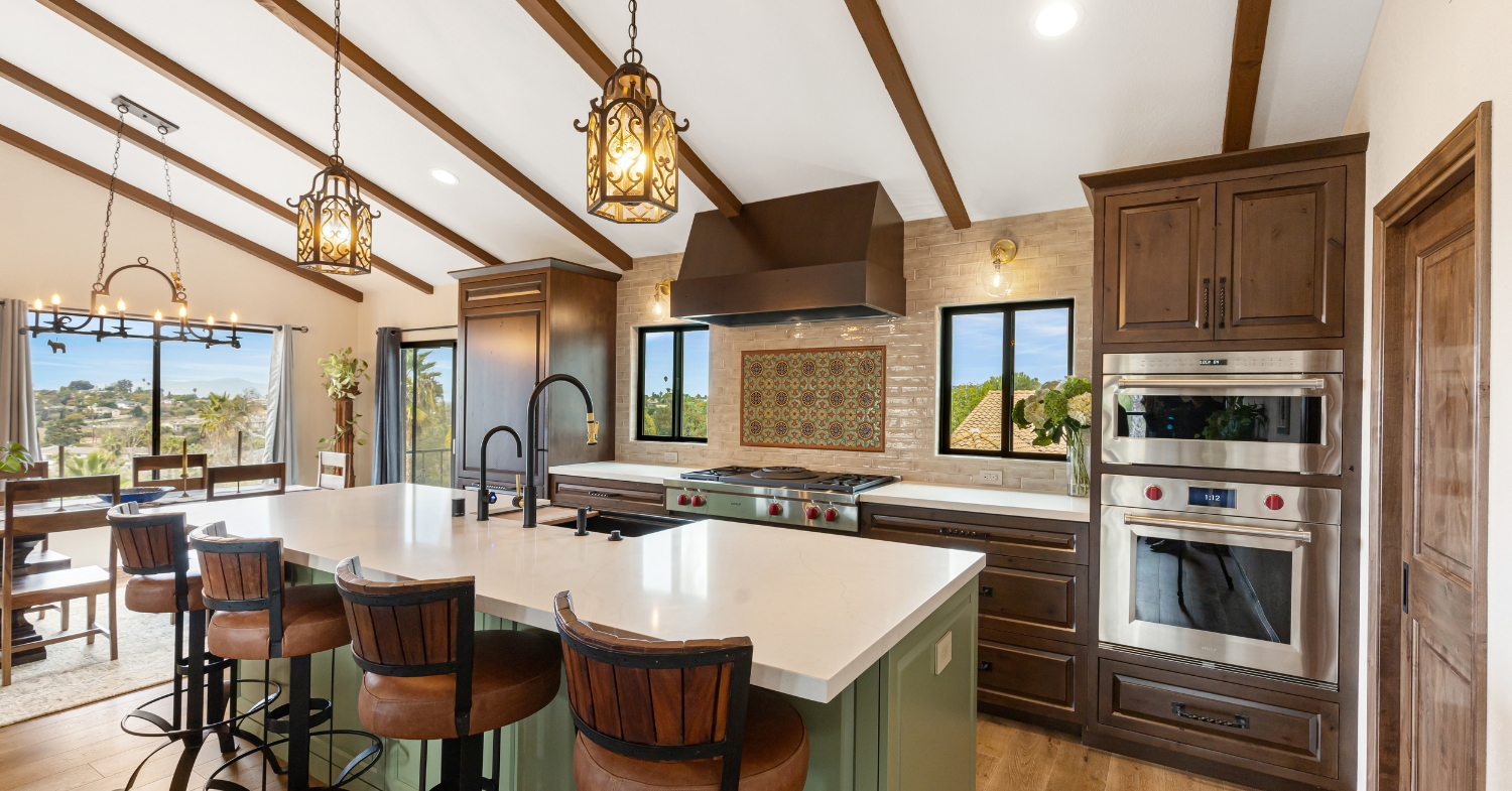 Luxury kitchen with dark custom cabinetry, exposed ceiling beams, a green island, professional appliances, and decorative pendant lights.