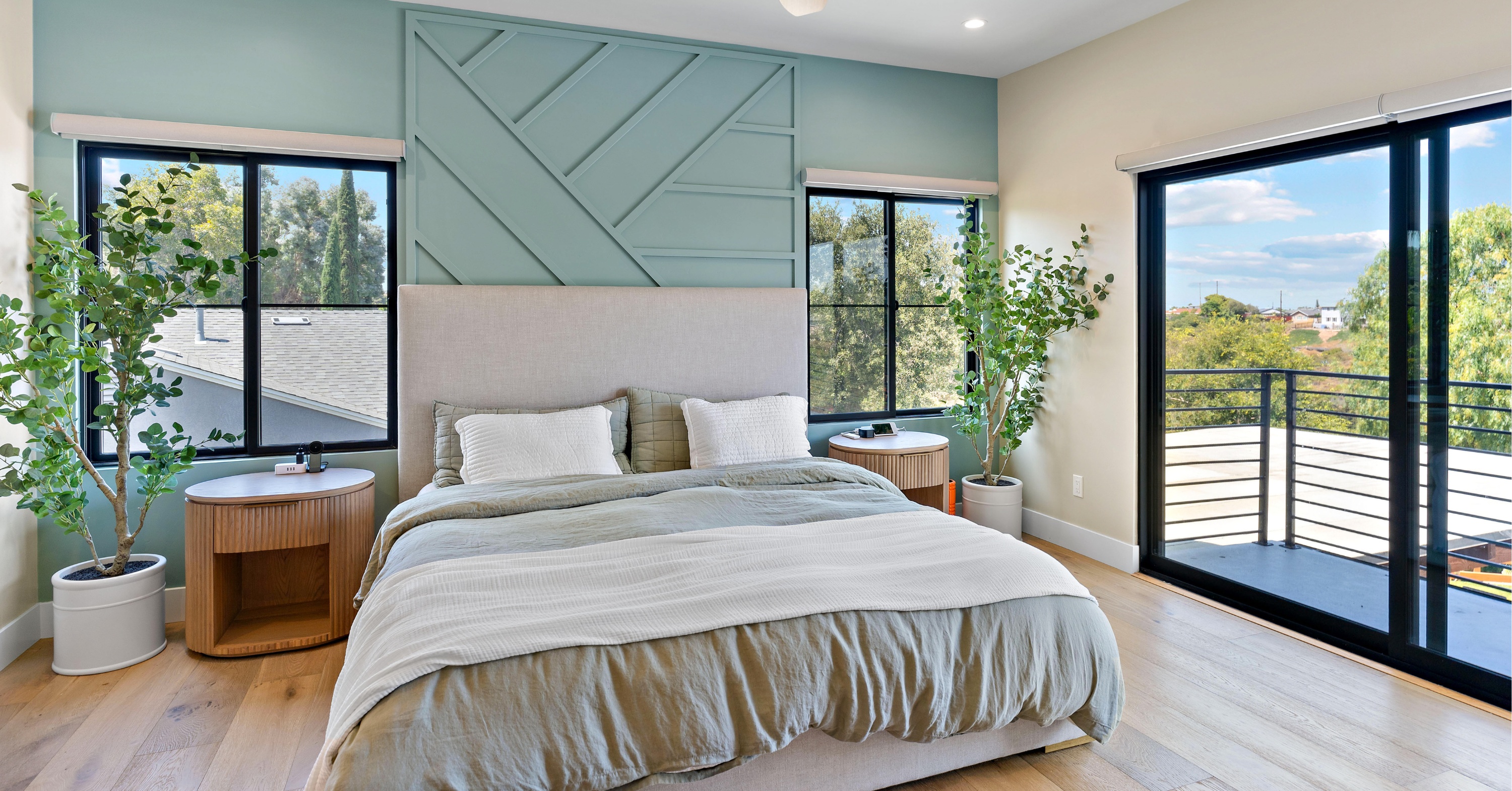 Contemporary master bedroom with a custom accent wall, spacious layout, balcony access, and oversized windows designed to maximize natural light.