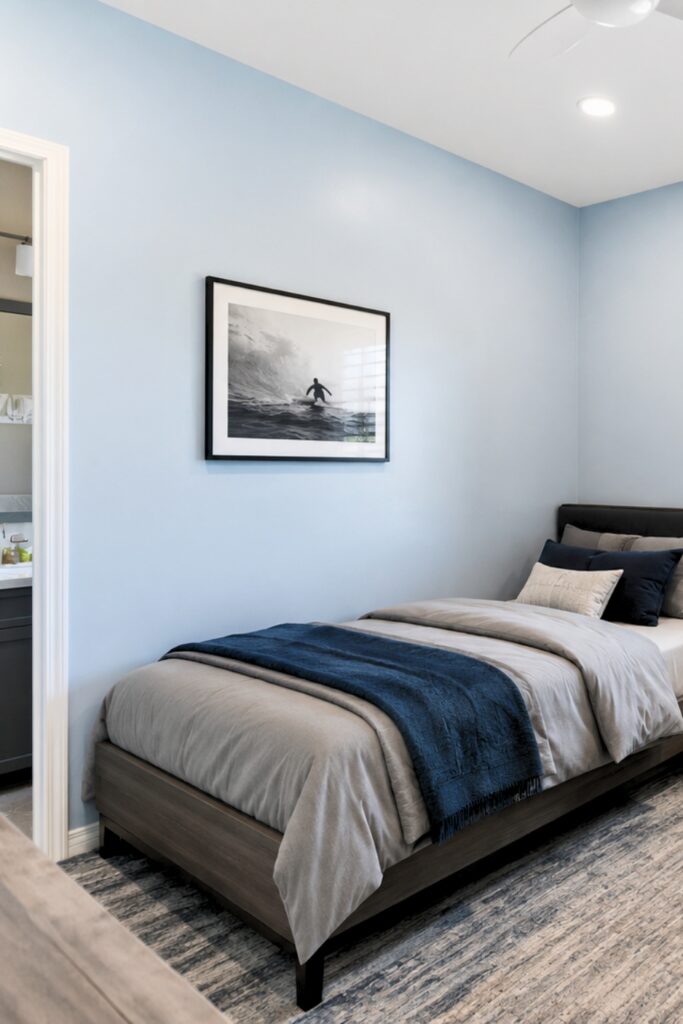 Blue bedroom with a dark wood bed, navy bedding, recessed lighting, and an attached bathroom doorway.
