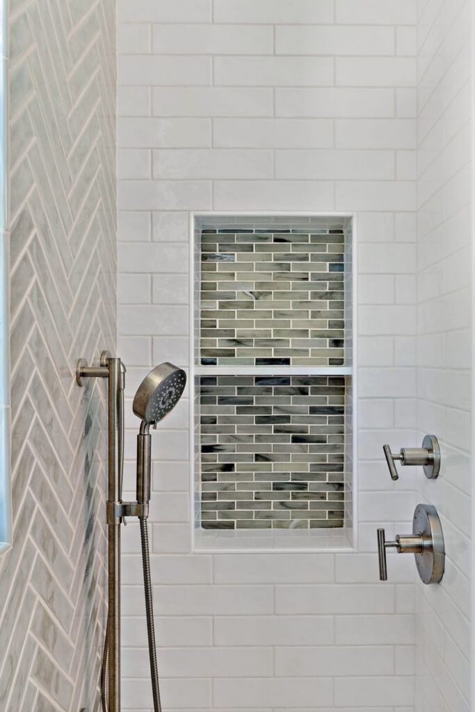 White subway tile shower wall with two built-in niches finished in gray and green glass mosaic tile.
