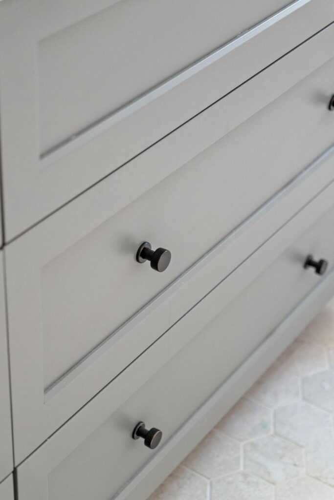 Close-up of gray bathroom vanity drawers with dark round cabinet knobs and inset panel fronts.