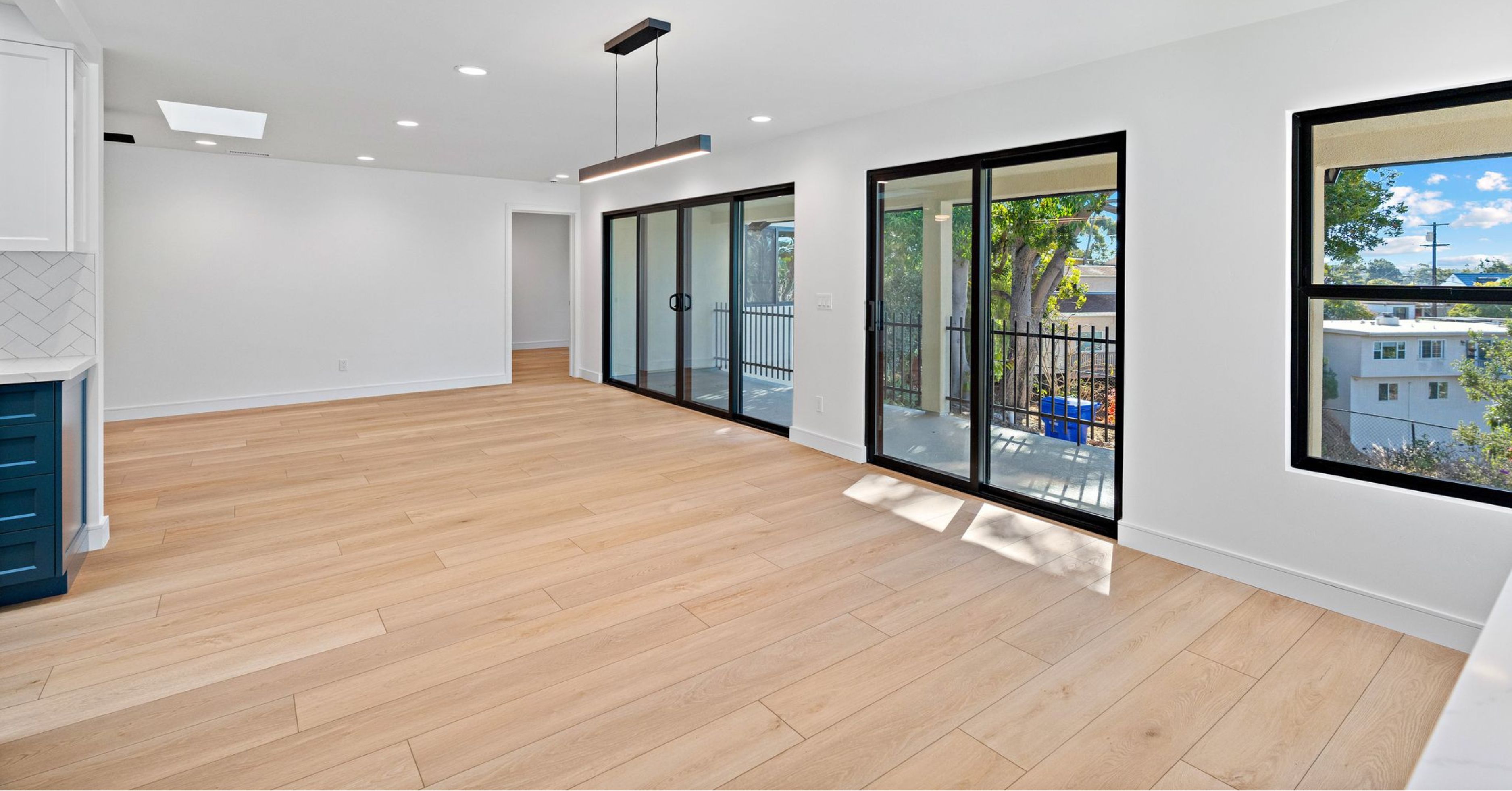 Bright open-concept living space with wide-plank wood flooring, large sliding glass doors, and abundant natural light after a whole-home renovation.