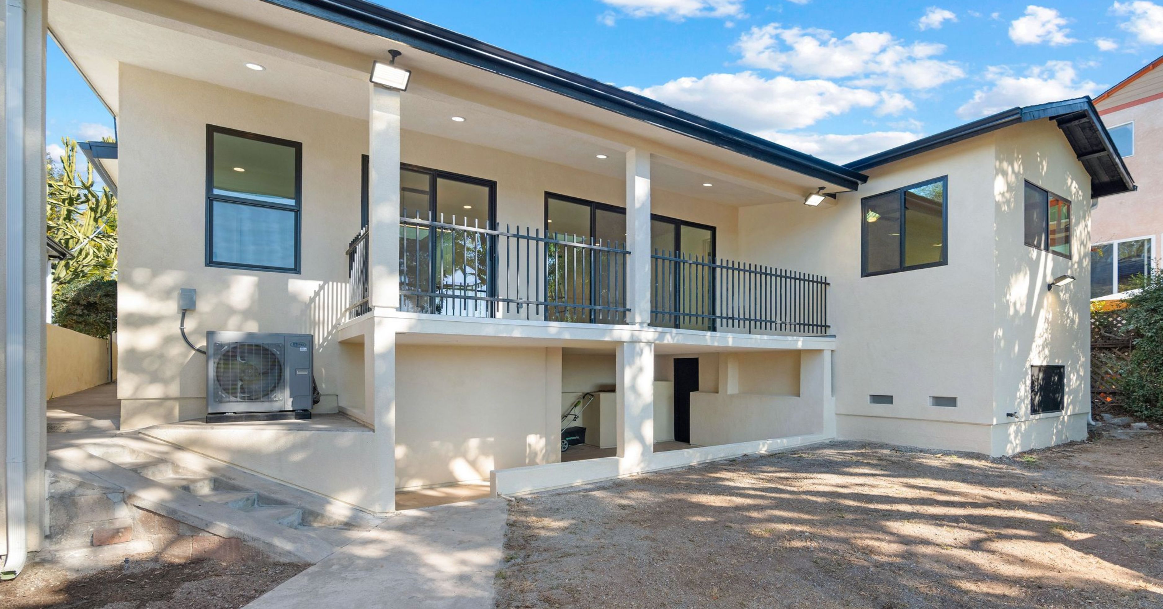 Rear exterior of a renovated San Diego home with covered patio, black-framed windows, sliding glass doors, and updated stucco finish.